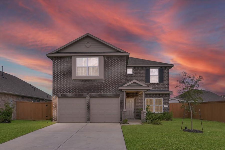 This is a two-story, brick-faced suburban home featuring a double garage and a neatly landscaped yard, set against a dramatic sunset sky.