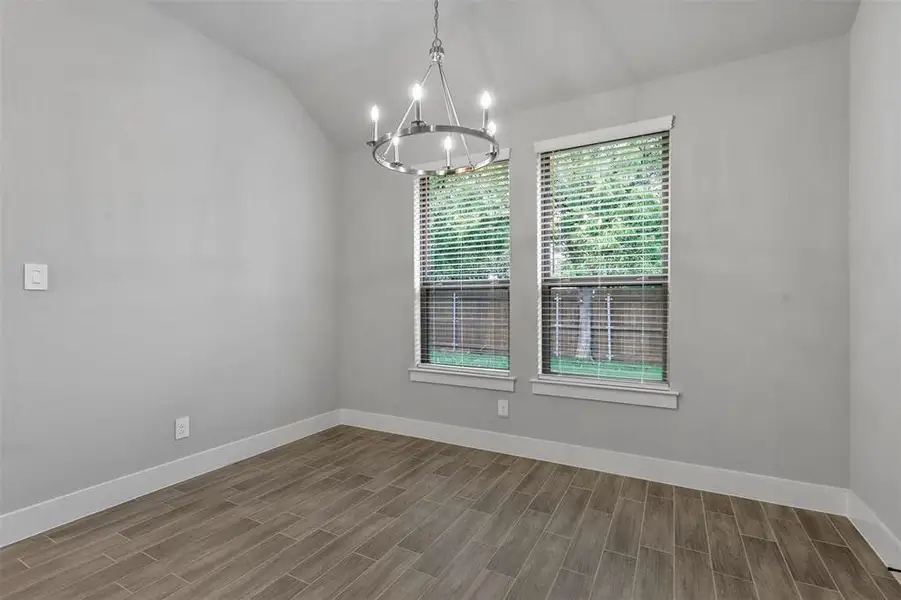 Unfurnished room featuring hardwood / wood-style floors, a chandelier, and vaulted ceiling