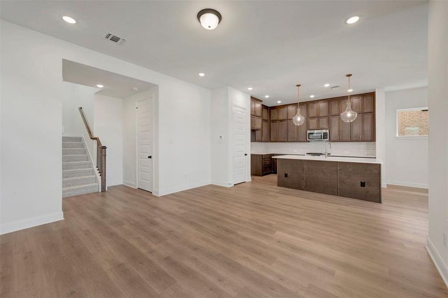Open-concept living space featuring wood-finish flooring, recessed lighting, a modern kitchen with dark wood cabinetry, a central island with white countertop, and stainless steel appliances
