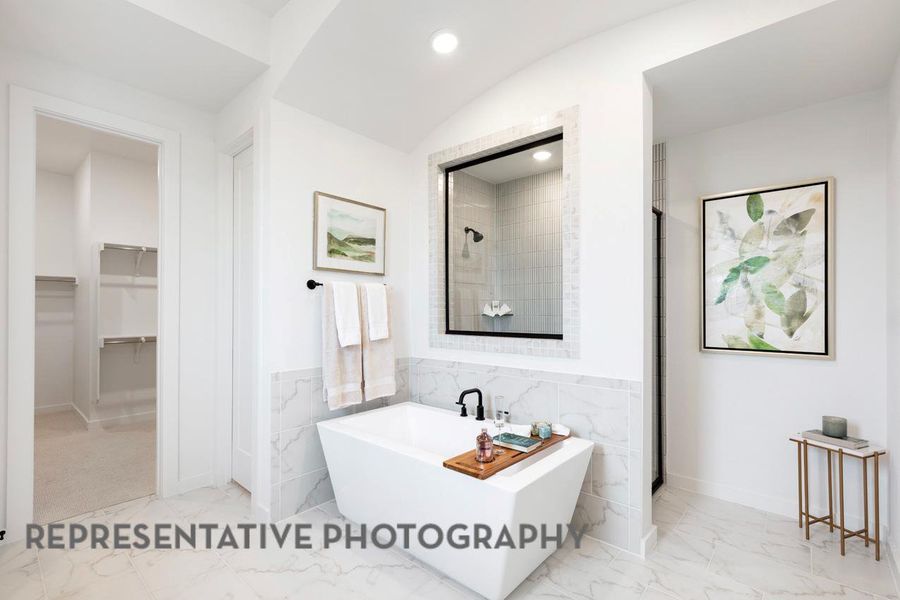 Bathroom featuring marble finish floors, a soaking tub, a spacious closet, lofted ceiling, and a shower Bathroom featuring marble finish floors, a soaking tub, a spacious closet, lofted ceiling, and a shower