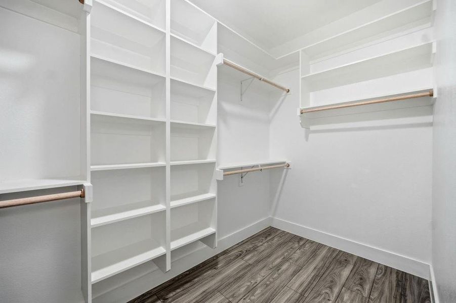 Spacious walk-in closet featuring extensive built-in shelving, multiple hanging rods, clean white finishes, and wood-finish flooring Spacious walk-in closet featuring extensive built-in shelving, multiple hanging rods, clean white finishes, and wood-finish flooring