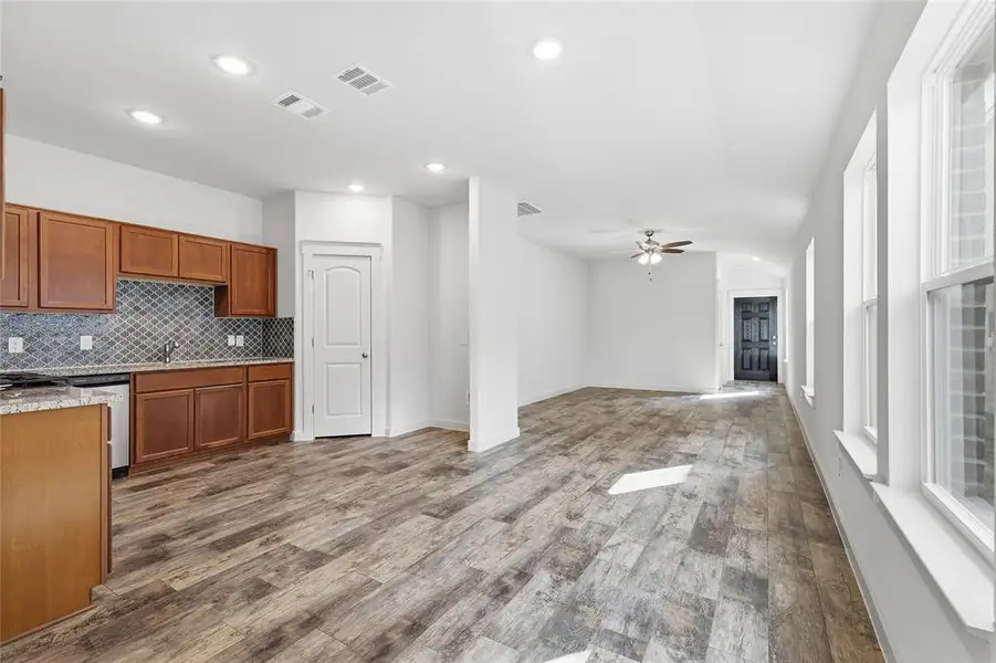 Kitchen with brown cabinetry, light stone counters, dishwasher, tasteful backsplash, and wood finished floors Kitchen with brown cabinetry, light stone counters, dishwasher, tasteful backsplash, and wood finished floors