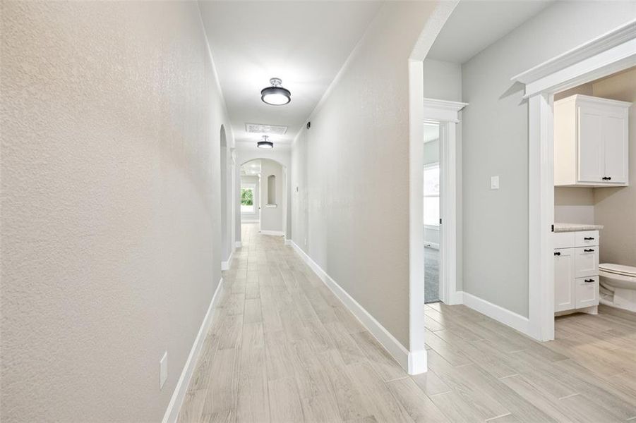 Hall featuring arched walkways, light wood-type flooring, and a textured wall Hall featuring arched walkways, light wood-type flooring, and a textured wall