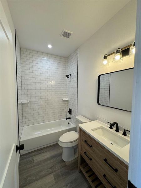 Full spare bathroom with tiled shower / bath, toilet, vanity, and hardwood / wood-style flooring