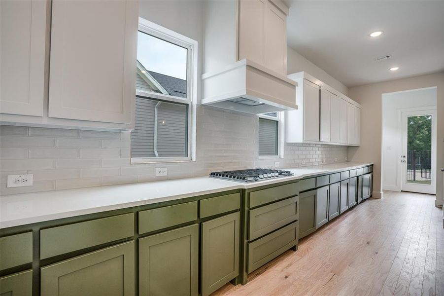 Kitchen with stainless steel gas stovetop, light hardwood / wood-style floors, white cabinets, and tasteful backsplash