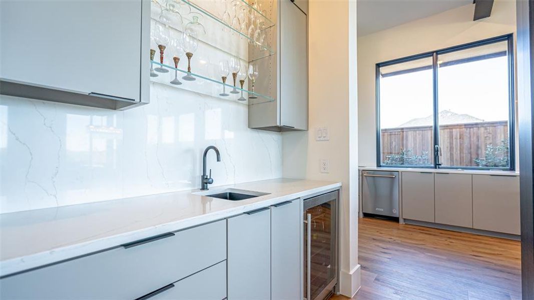 Kitchen with gray cabinetry, light stone counters, sink, and beverage cooler