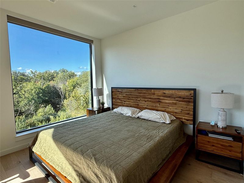 Floor-to-ceiling windows offer serene treetop views in this primary bedroom retreat.