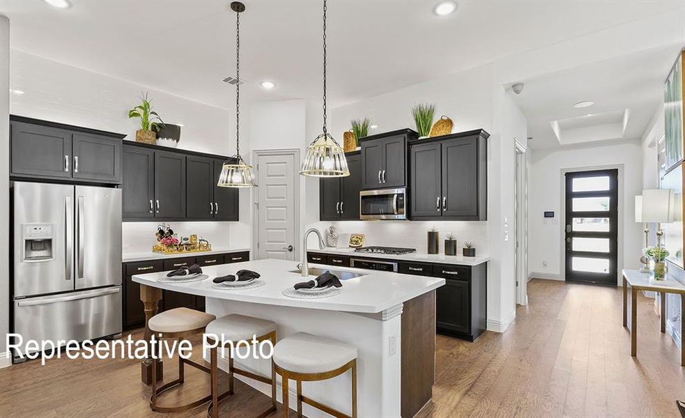 Kitchen with appliances with stainless steel finishes, wood-type flooring, an island with sink, pendant lighting, and a breakfast bar