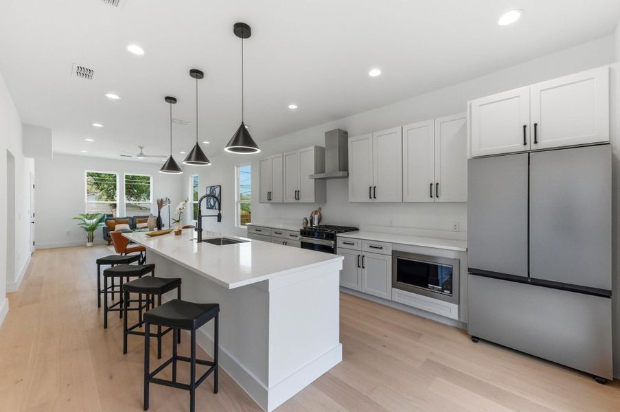 Kitchen with appliances with stainless steel finishes, recessed lighting, hanging light fixtures, a center island with sink, and wall chimney exhaust hood