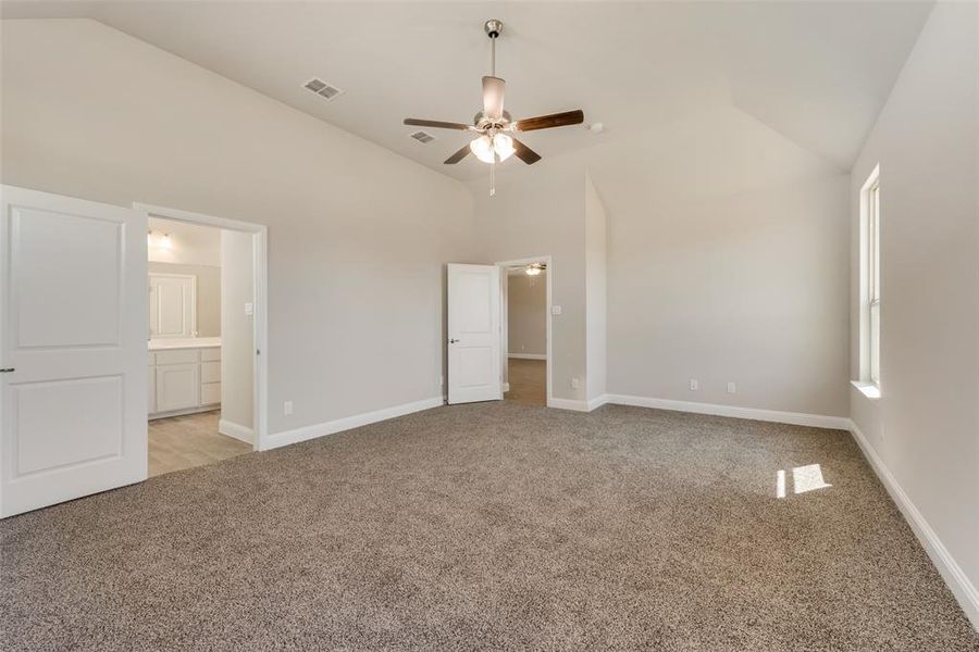 Primary bedroom with ceiling fan, light colored carpet, ensuite bathroom, and high vaulted ceiling