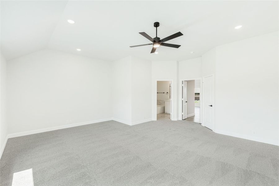 Spacious bedroom with gray carpet, vaulted ceiling, black ceiling fan, and open ensuite bathroom door