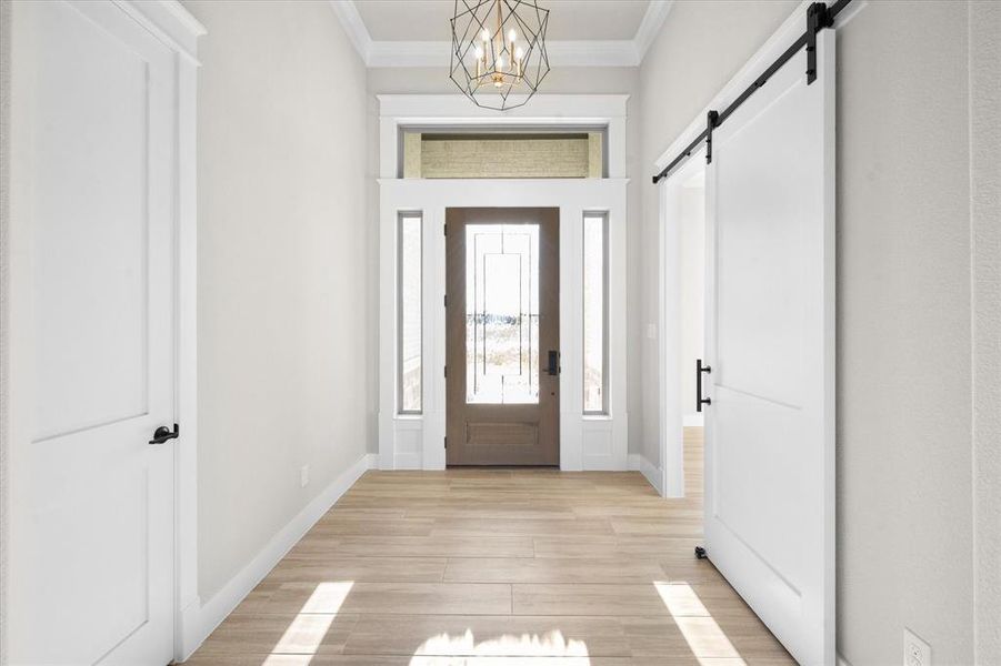 Entrance foyer with a barn door, light hardwood / wood-style floors, an inviting chandelier, and ornamental molding