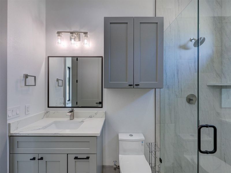Modern stone countertops and a glass-enclosed walk-in shower highlight this sleek bathroom space.