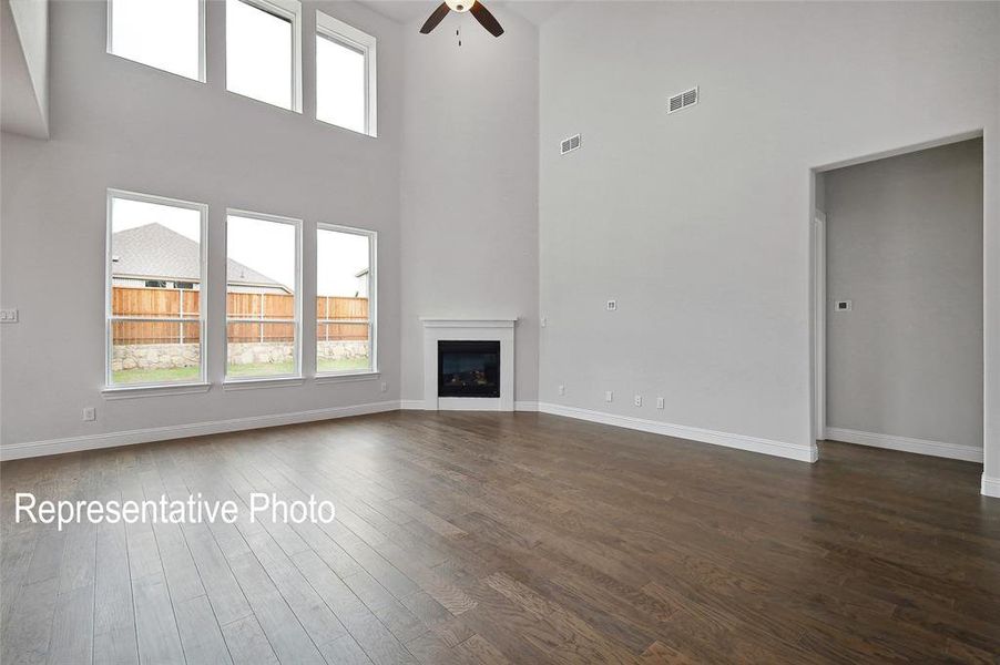 Two-story living area featuring tall windows, a corner fireplace with a white mantel, and dark wood-finish flooring