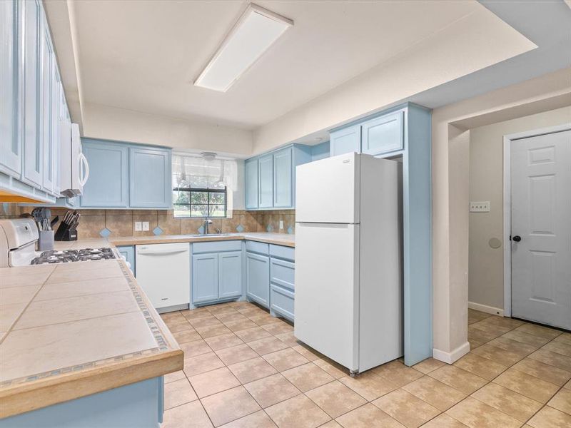 Kitchen with white appliances, blue cabinets, and light tile patterned floors Kitchen with white appliances, blue cabinets, and light tile patterned floors