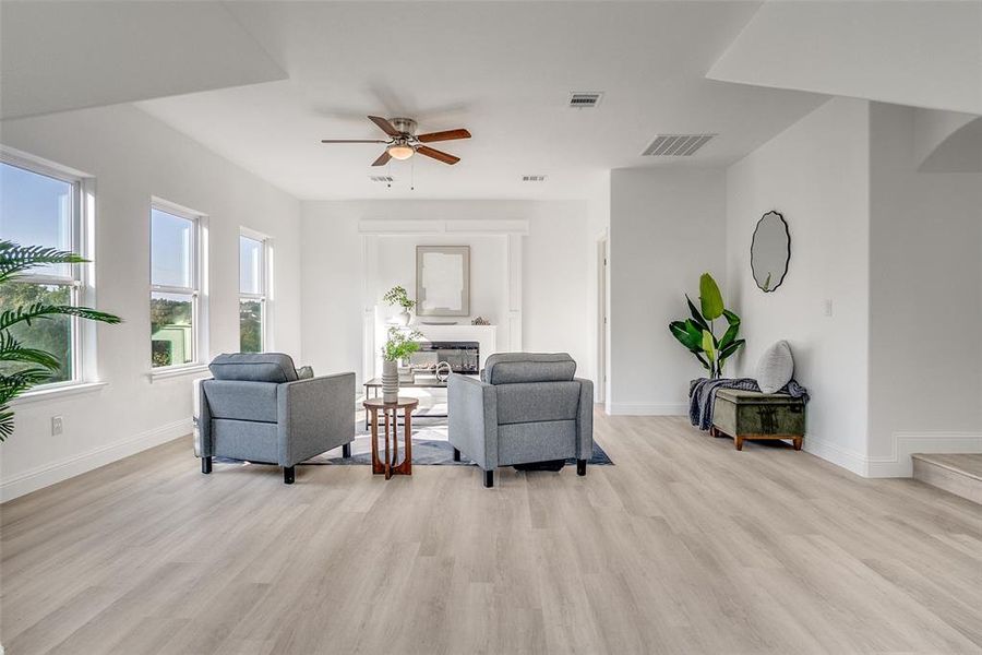 Living area featuring ceiling fan, light wood-style floors, and a glass covered fireplace Living area featuring ceiling fan, light wood-style floors, and a glass covered fireplace