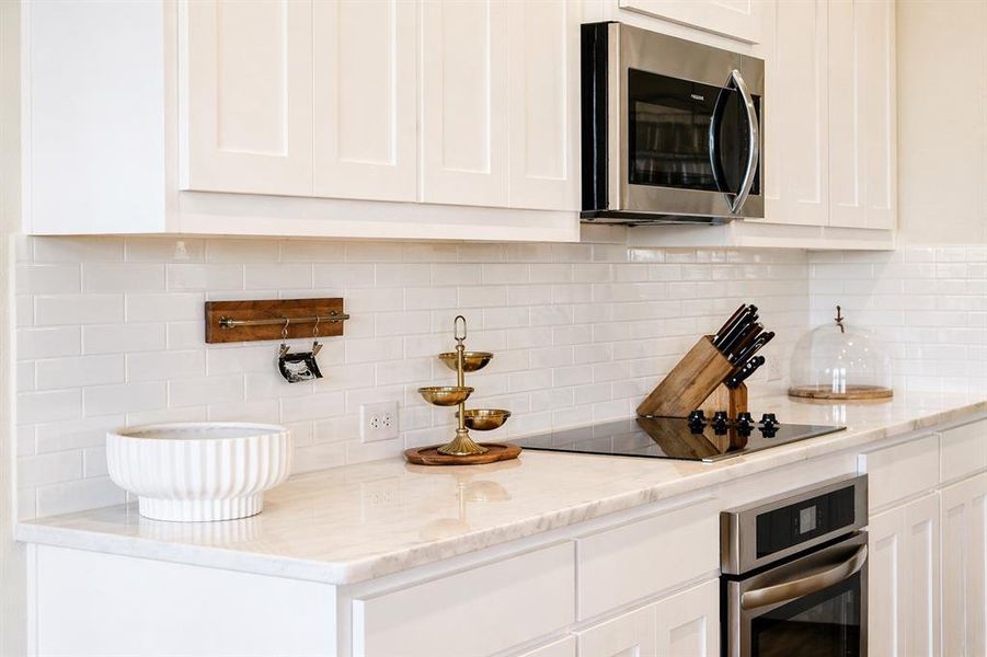 Modern kitchen featuring white shaker cabinetry, light-toned countertops, a white subway tile backsplash, stainless steel microwave, and a flush-mounted cooktop