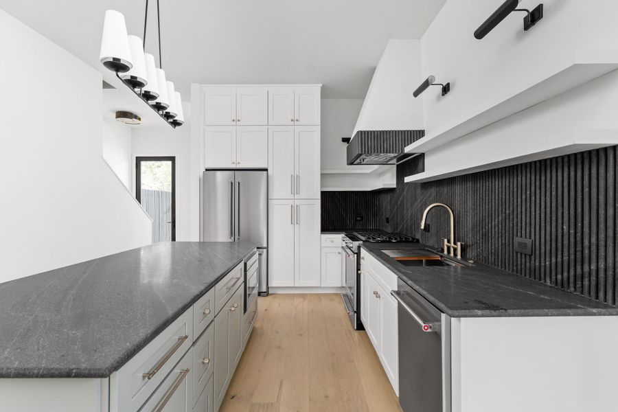 Kitchen with appliances with stainless steel finishes, white cabinets, light wood-type flooring, tasteful backsplash, and dark stone countertops
