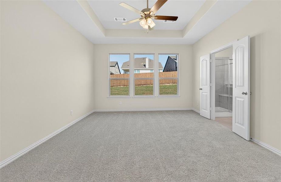 Unfurnished bedroom with light carpet, ensuite bath, a raised ceiling, and ceiling fan