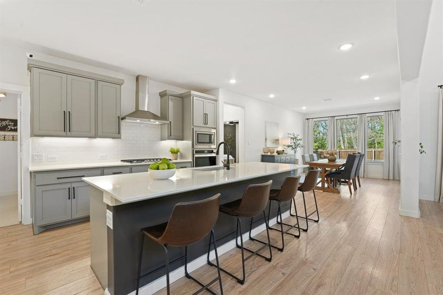 Kitchen with gray cabinetry, a kitchen island with sink, wall chimney range hood, recessed lighting, and light stone counters