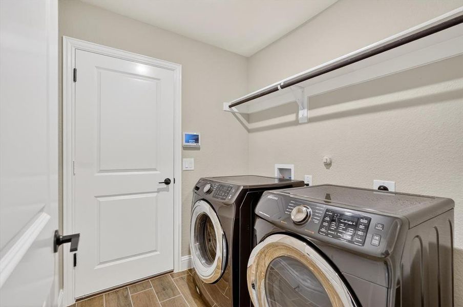 Dedicated laundry area featuring wood-finish flooring, light neutral wall paint, and a built-in hanging rod Dedicated laundry area featuring wood-finish flooring, light neutral wall paint, and a built-in hanging rod