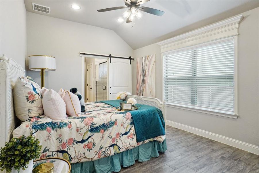 Bedroom with lofted ceiling, a barn door, hardwood / wood-style floors, ceiling fan, and ensuite bathroom