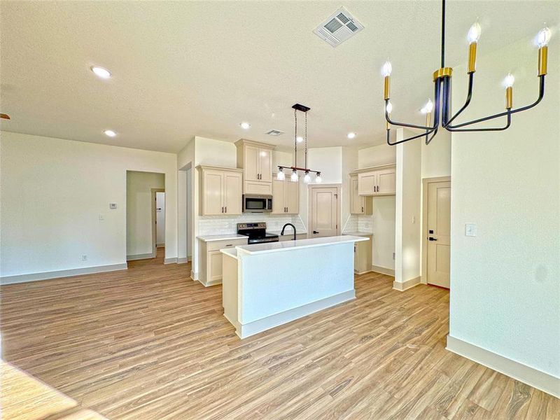 Kitchen featuring a chandelier, an island with sink, backsplash, pendant lighting, and light countertops