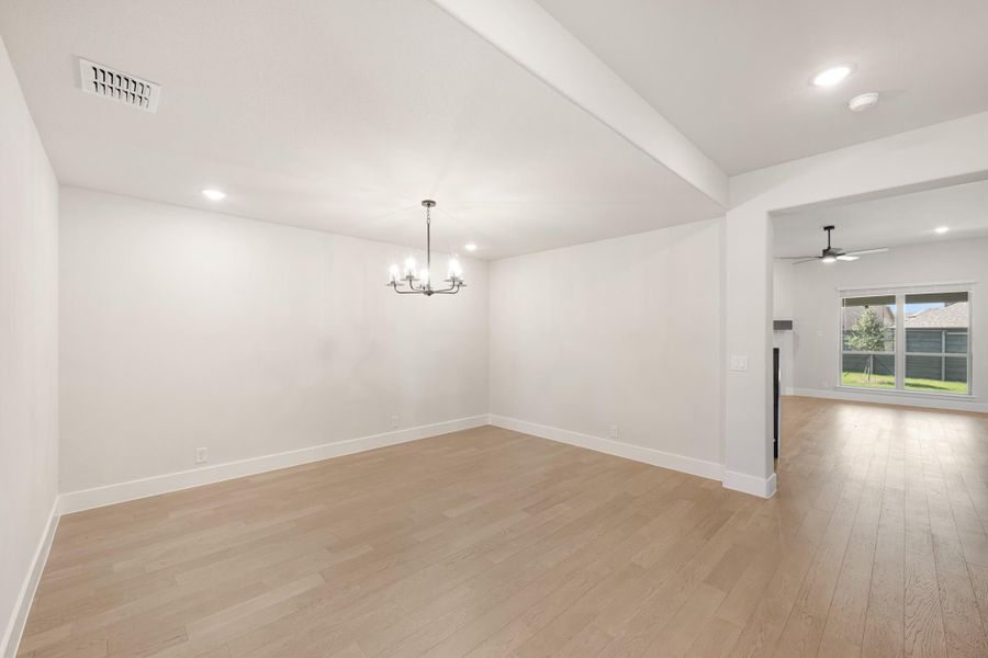 Empty dining room with chandelier and light hardwood floors, open to living area with ceiling fan and sliding glass door