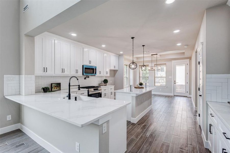 Kitchen with dark wood-style tiled floors, recessed lighting, appliances with stainless steel finishes, white cabinets, and custom backsplash