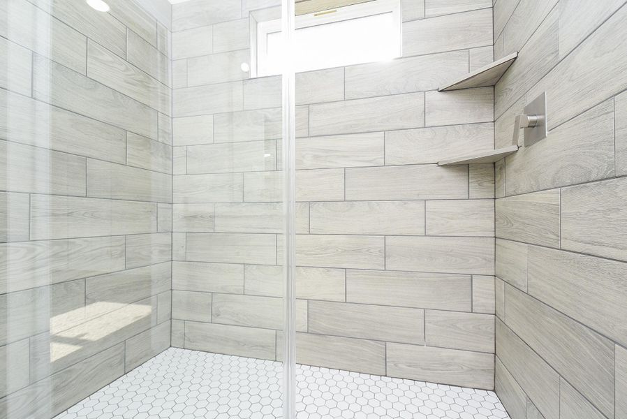 This is a modern walk-in shower with light wood-look tile walls, hexagonal floor tiles, and built-in shelving, showcasing a sleek and contemporary design. This is a modern walk-in shower with light wood-look tile walls, hexagonal floor tiles, and built-in shelving, showcasing a sleek and contemporary design.