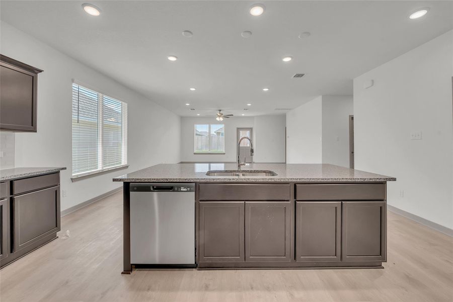 Kitchen featuring stainless steel dishwasher, light wood-style floors, recessed lighting, light stone countertops, and dark brown cabinets