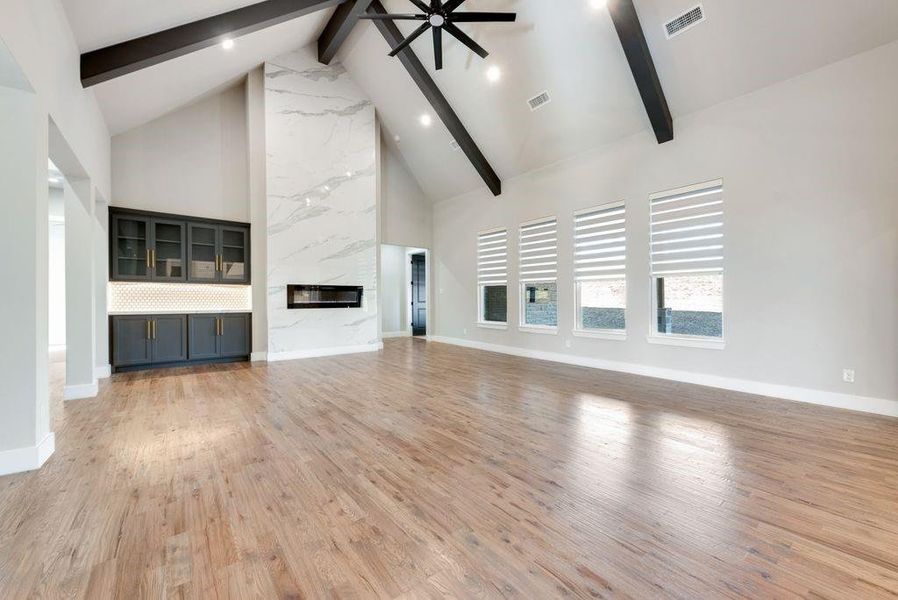 Unfurnished living room featuring a high end fireplace, high vaulted ceiling, light wood-type flooring, and beam ceiling