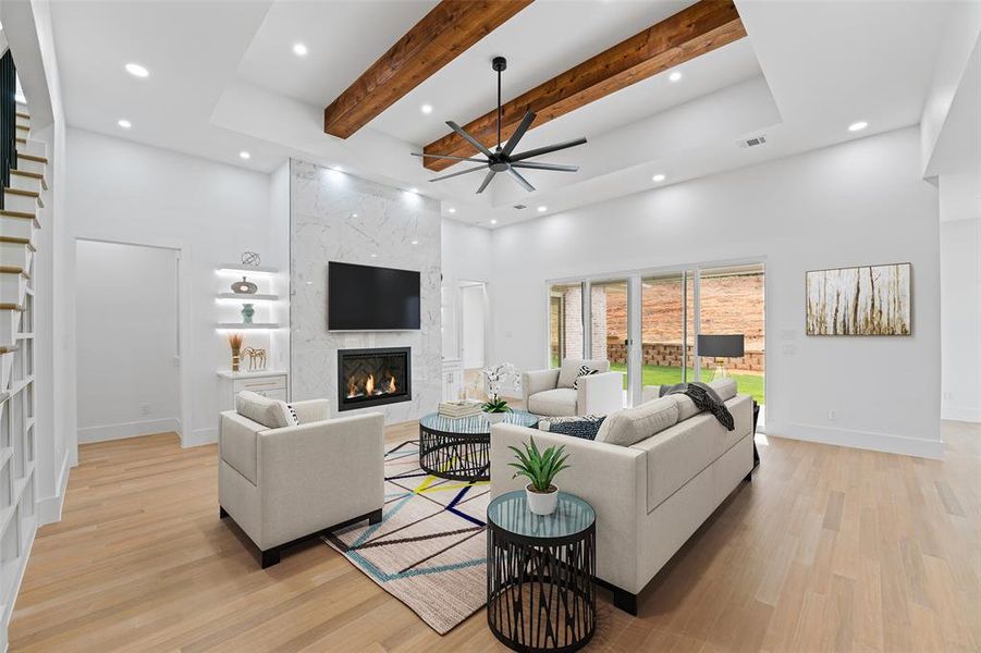Living room featuring a towering ceiling, beamed ceiling, ceiling fan, light wood finished floors, and a premium fireplace