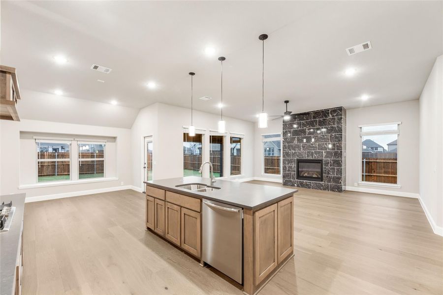 Open-concept kitchen with center island, pendant lights, and stone fireplace in adjoining living area