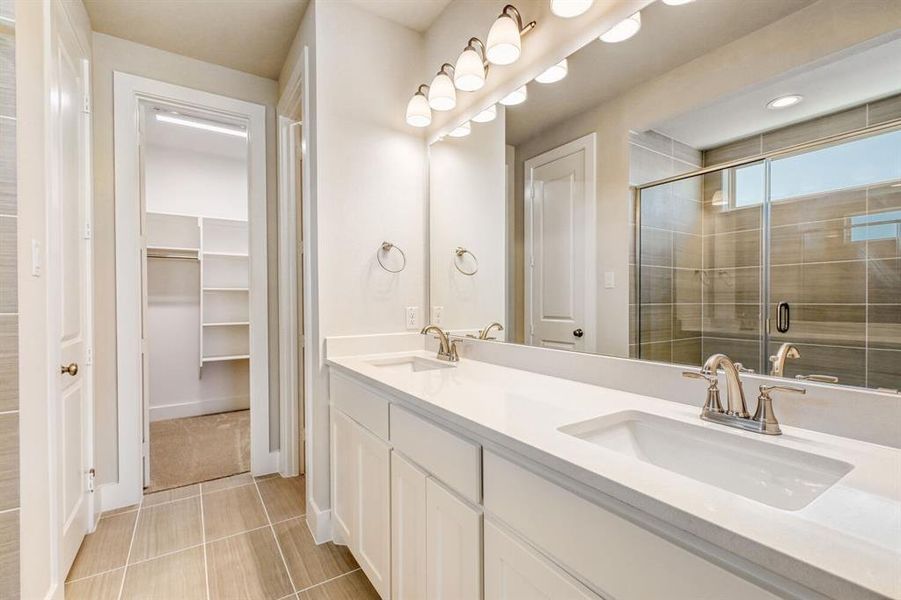 Full bathroom featuring double vanity, a stall shower, a spacious closet, and light tile patterned floors