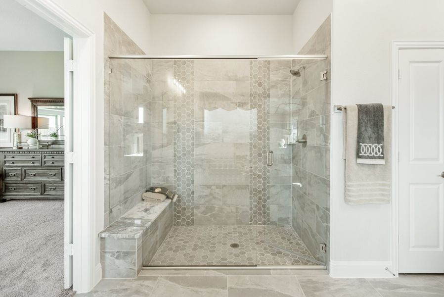 Walk-in shower with glass doors, gray marble tile walls, hexagon floor tile, and built-in bench seat