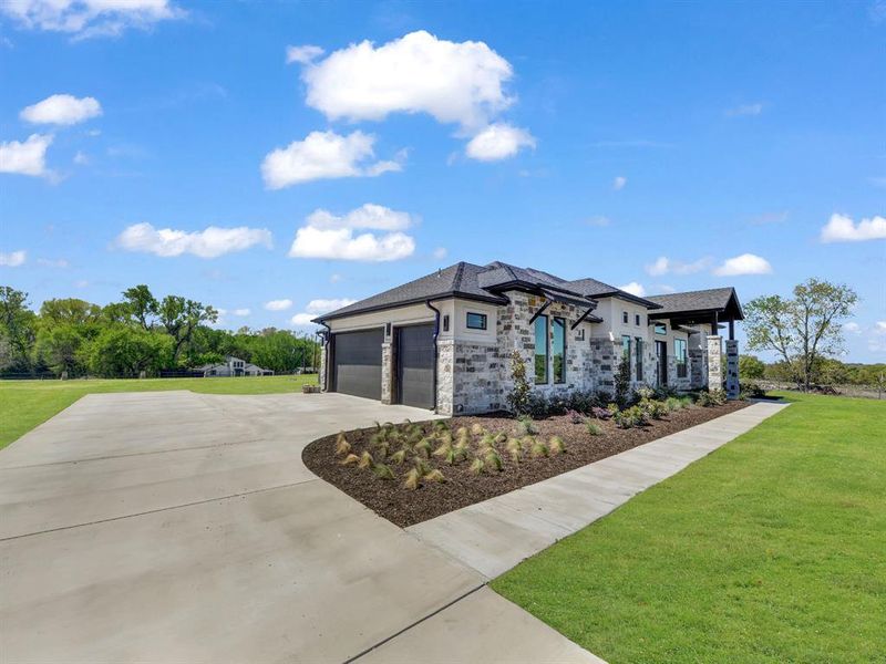 View of front of home with a front yard, stone siding, a garage, and driveway View of front of home with a front yard, stone siding, a garage, and driveway