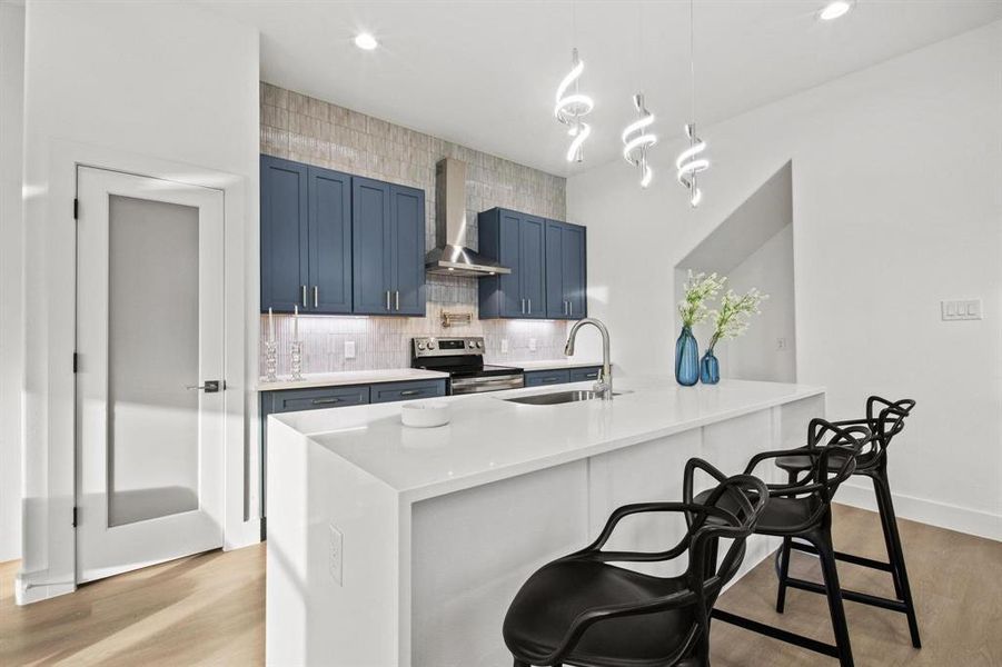 Kitchen featuring blue cabinets, a kitchen breakfast bar, light wood-type flooring, decorative backsplash, and hanging light fixtures