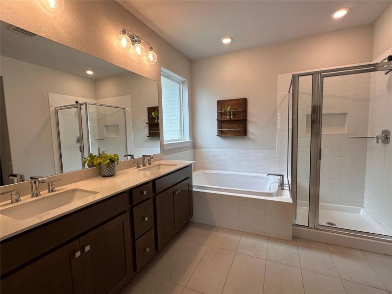 Primary bathroom featuring a dual vanity with light-toned countertops, a built-in soaking tub, and a glass-enclosed shower.