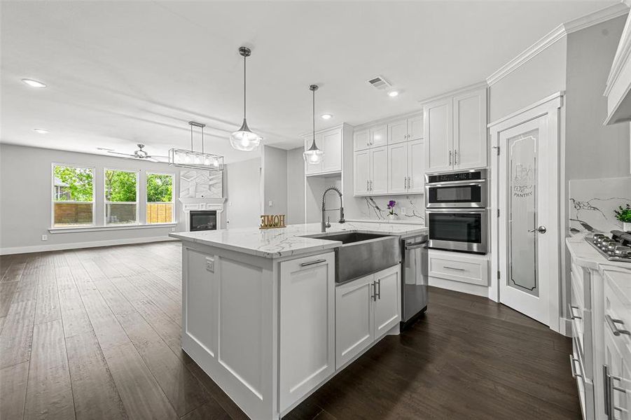 Kitchen with a kitchen island with sink, sink, decorative light fixtures, white cabinetry, and dark hardwood / wood-style flooring