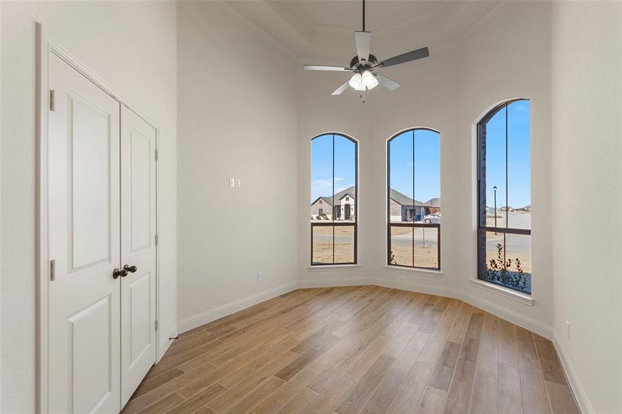 Empty room featuring light wood-type flooring, ceiling fan, ornamental molding, and a high ceiling Empty room featuring light wood-type flooring, ceiling fan, ornamental molding, and a high ceiling