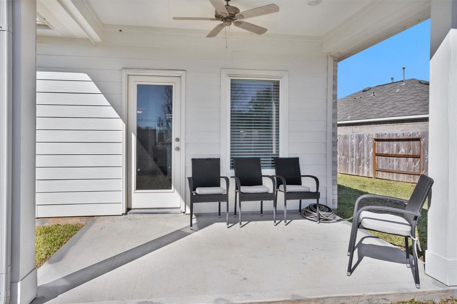 This covered back patio features a ceiling fan, and easy access to the backyard, creating a relaxing space for outdoor dining and entertaining.