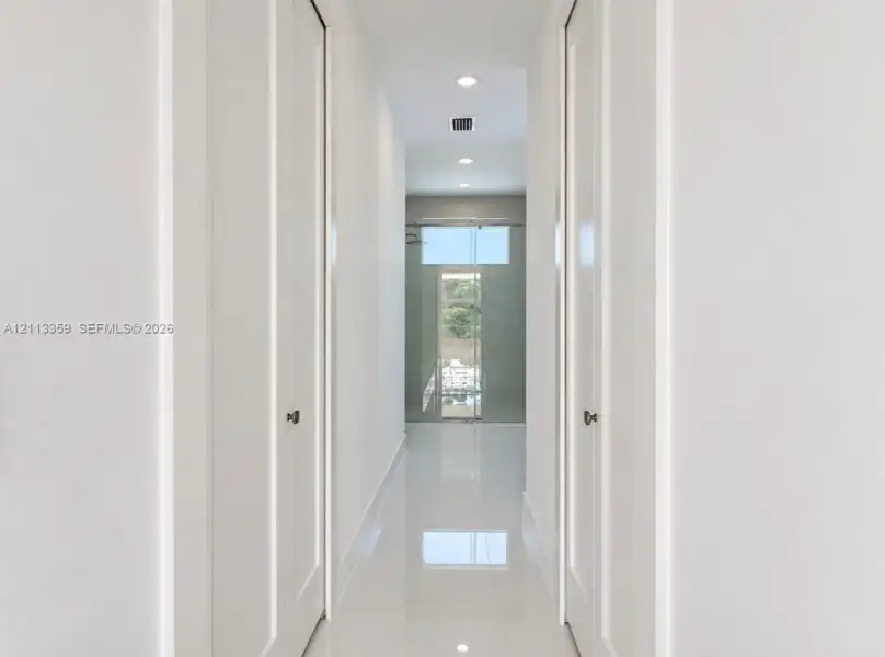 Hallway featuring high-gloss tile flooring, recessed ceiling lighting, and dual floor-to-ceiling closets with paneled doors