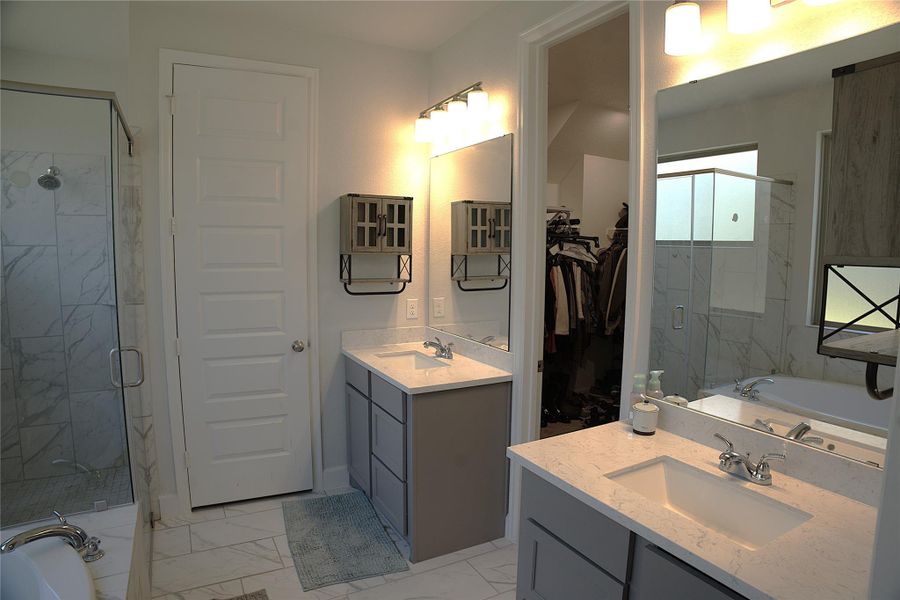 Bathroom featuring a bath, a marble finish shower, light marble finish flooring, two vanities, and a spacious closet Bathroom featuring a bath, a marble finish shower, light marble finish flooring, two vanities, and a spacious closet