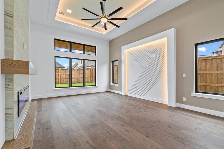 Unfurnished living room featuring a premium fireplace, ceiling fan, a tray ceiling, and wood-type flooring