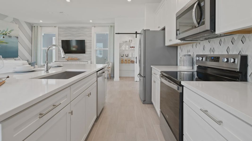 Open kitchen with white cabinets and large island at a DRB Homes Ambersweet model at the Trinity Place community. Open kitchen with white cabinets and large island at a DRB Homes Ambersweet model at the Trinity Place community.
