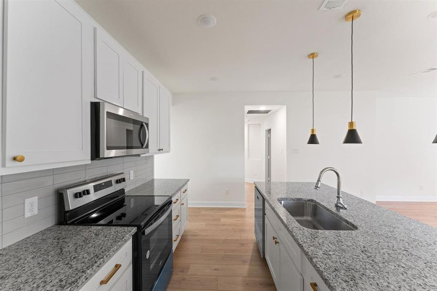 Kitchen featuring stainless steel appliances, sink, light stone countertops, white cabinetry, and light hardwood / wood-style floors