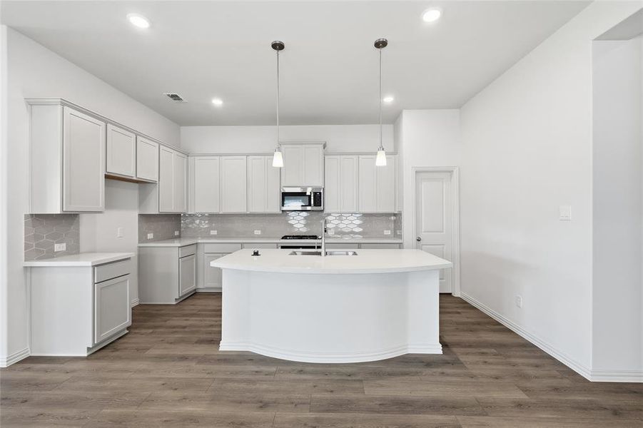 Kitchen with decorative light fixtures, stainless steel microwave, dark wood finished floors, an island with sink, and decorative backsplash
