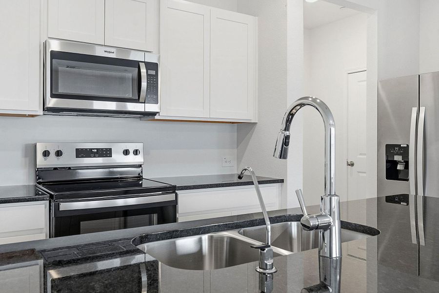 Stainless steel kitchen appliances, including an over-the-range microwave and electric range, complement dark stone countertops Stainless steel kitchen appliances, including an over-the-range microwave and electric range, complement dark stone countertops