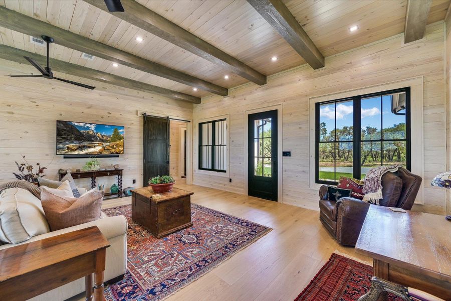 Living area with wood walls, a barn door, light wood-style flooring, a ceiling fan, and recessed lighting